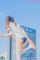 A woman in a white shirt and blue shorts is jumping in the air.