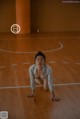 A woman in a white shirt is crouching on a wooden floor.