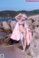 A woman in a bikini standing on a beach next to the ocean.