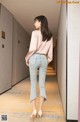 A woman in a pink blouse and jeans walking down a hallway.