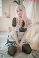 A woman with long pink hair sitting on a bed.