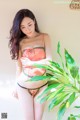 A woman in a pink lingerie posing next to a plant.