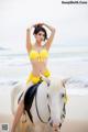 A woman in a yellow bikini riding a white horse on the beach.