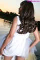 A woman in a white dress standing by a body of water.