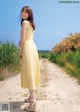 A woman in a yellow dress standing on a dirt road.