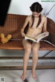 A naked woman sitting on a bench reading a book.