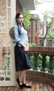 A woman in a blue shirt and black skirt standing on a balcony.