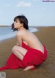 A woman in a red dress sitting on the beach.