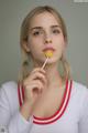 A woman holding a yellow lollipop in her mouth.