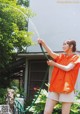 A woman in an orange shirt is holding a hose.