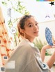 A woman holding a blue fan in front of a window.