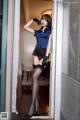 A woman in a blue shirt and black stockings posing in a doorway.